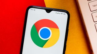 オレンジと赤の表面に置かれた Android スマートフォンに表示される Google Chrome ロゴ
