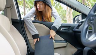車の前部座席からラップトップを取り出すパーカーを着た若い女性。