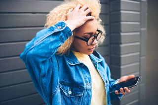 電話を見ながらイライラして髪を掴む若い女性。