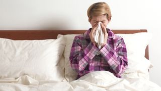 短いブロンドの髪の女性は、アレルギーのため夜間のいびきが悪化するため、ベッドで鼻をかんでいます。