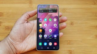 誰かの手にある Samsung Galaxy S21 FE 5G、その後ろに木製の表面がある