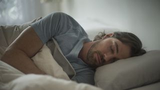長い黒髪の男性はいびきをかく可能性を減らすためにベッドで横向きに寝ています