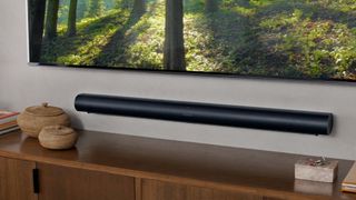 森林の風景を表示する大型の壁掛けテレビの下にある壁掛けの Sonos Arc。