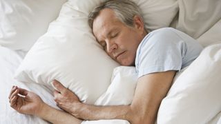 よりよく眠る方法: 白い掛け布団に覆われたベッドで眠っている白髪の中年男性