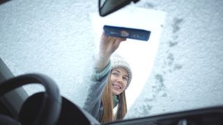 車のフロントガラスの霜取りをする女性