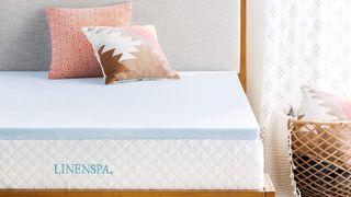 画像は、日当たりの良い寝室の木製ベッドフレームに Linenspa 3 インチのジェル注入メモリーフォームマットレストッパーを取り付けたものです。