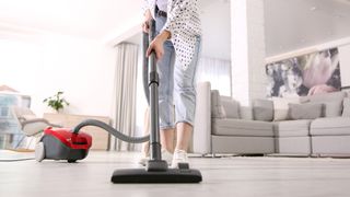 シリンダー掃除機を使って家の固い床を掃除する若いうめき声